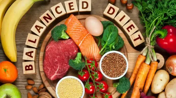 A photo of fruits, vegetables, nuts et cetera different kinds of food in a frame. "Balanced Diet" is written on wooden blocks suggesting balanced diet for International Yoga Day 2023.
