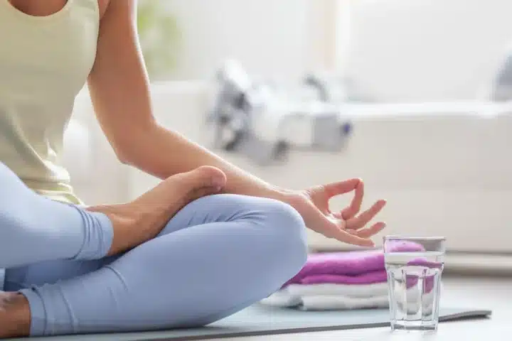 A photo of a Woman doing Yoga and sitting in a pose. A glass of water is beside her suggesting hydration while doing yoga on International Yoga Day 2023.