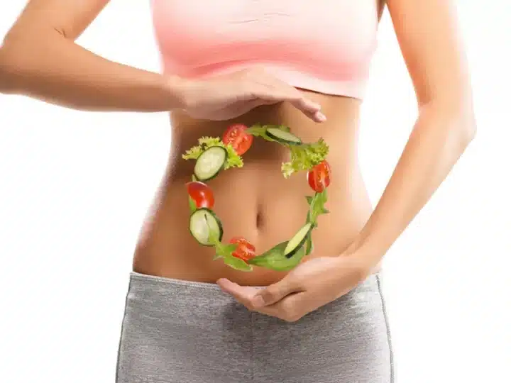 Yoga and Digestion A photo of a woman standing with her hands in a magician like gesture around a chakra like circle made up of tomatoes, salad dressing and cucumber suggesting Pre and Post Yoga Meals for International Yoga Day 2023.