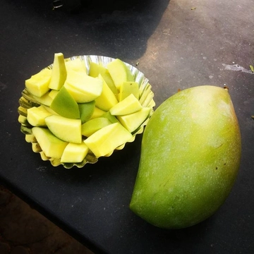 A Totapuri Mango with a plate on side that holds finely-cut pieces of Totapuri Mango