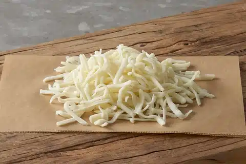 Shredded Mozzarella Cheese on a cloth on a wooden bench.