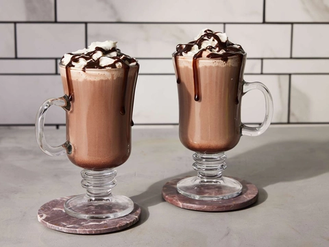 An image of two mouth-watering cocoa drinks served in glasses with ice cream and chocolate syrup on top.