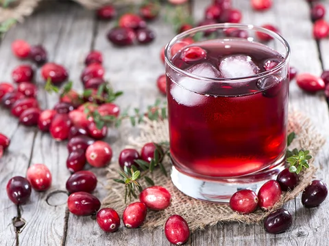 An image of Cranberry juice in a glass surrounded by cranberries.