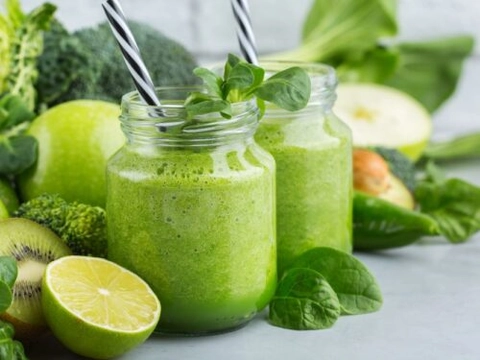 Image of Green Smoothies in jars. They are covered by green veggies, fruits and leaves.