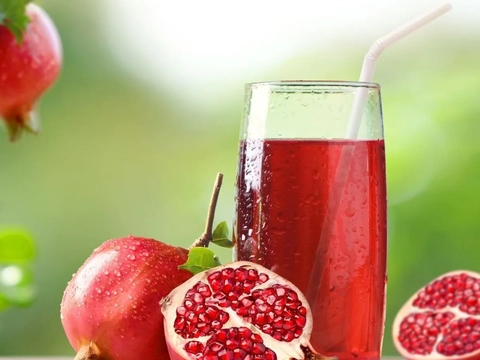 An image of Pomegranate Juice served in a glass with straw. There are Pomegranates surrounding it.