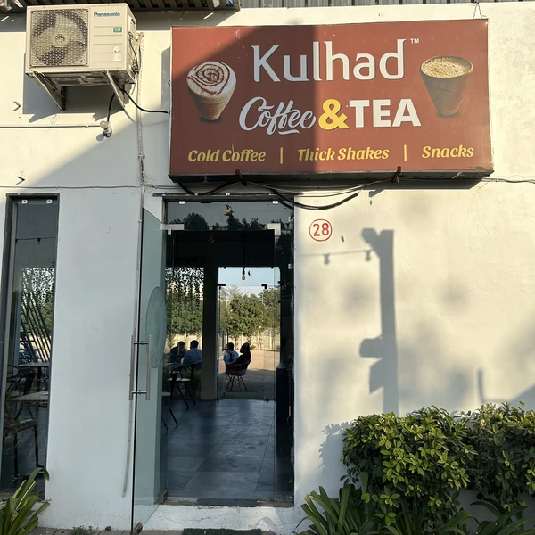 An image of Kulhad Coffee & Tea. The image features red board and food and tea. The door is open and the wide open seating area is visible.